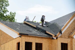 A homeowner inspects gutters beside a residential roof while autumn leaves gather below.